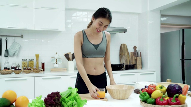 年轻的亚洲妇女步行到厨房和喝橙汁在早上的周末。健康饮食和健康生活方式的概念。视频素材
