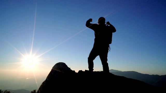 SLO MO Man站在山上，对着日出的天空举起双臂。视频素材