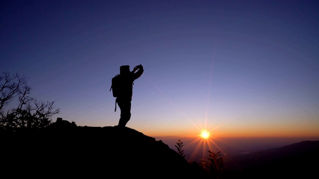 一个背包客在日出的时候用他的手机在山顶拍照。视频素材