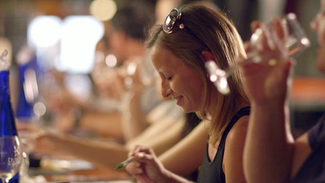 在一家酒厂的品酒活动中，一名年轻女子抿着一杯葡萄酒，兴奋地写着笔记视频素材