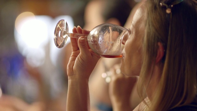 在一家酒厂的品酒活动上，一名年轻女子微笑着旋转着一杯玫瑰葡萄酒，然后抿了一口。视频下载