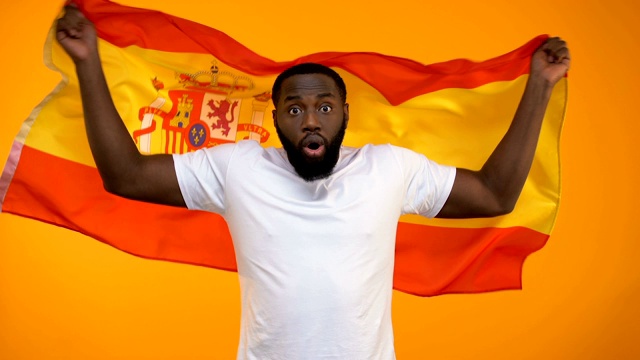惊讶的非洲裔美国体育迷挥舞着西班牙国旗，为胜利欢呼视频素材