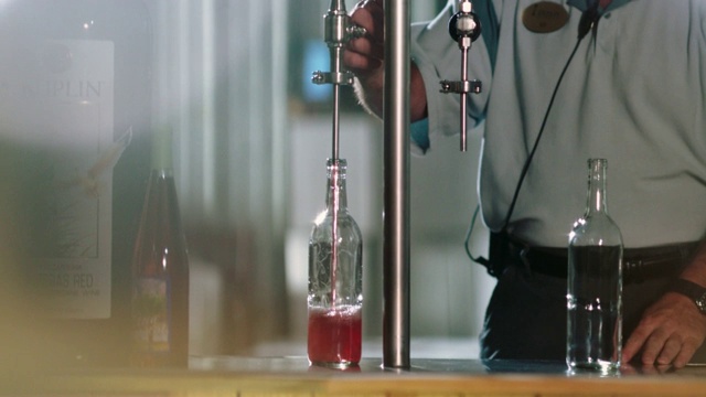 酿酒厂员工用喷瓶机将一个干净的瓶子装满玫瑰色的葡萄酒。视频素材