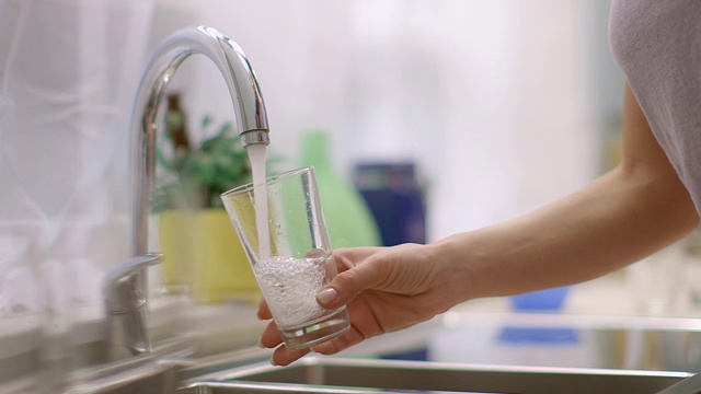 年轻女子在厨房里用水龙头往杯子里注水。视频下载
