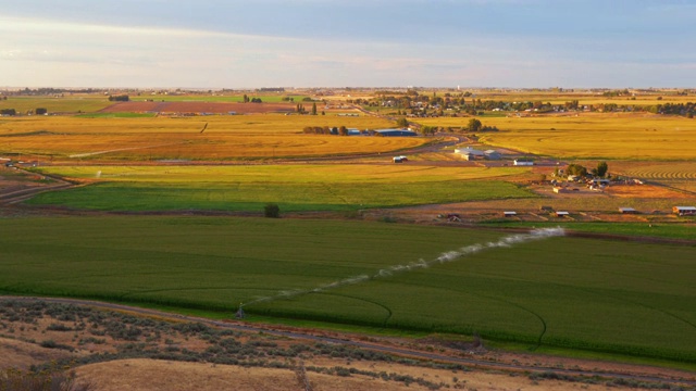 延时镜头在广阔的地平线上拍摄，展现了小型农业社区和绿色灌溉农田。视频素材
