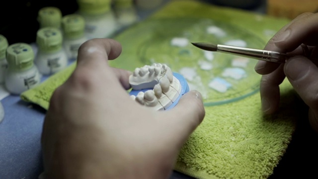牙科技师为病人从零开始制造新牙齿。牙科医生在牙科诊所用牙科设备在昏暗的光线下固定牙齿。牙医准备牙齿。视频素材