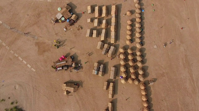 头顶无人机拍摄的稻草小屋和木平房散布在沙滩上视频素材