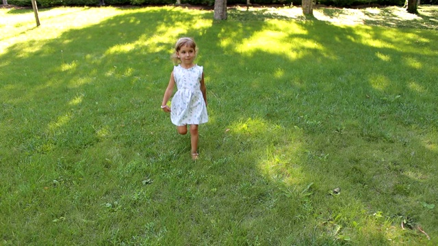 一个快乐的四岁小女孩在公园的绿草地上跑步。视频素材