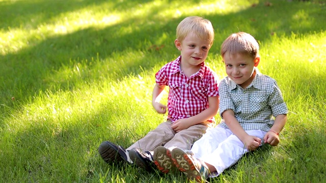 两个有趣的小男孩在公园的草地上玩耍，他们坐在草地上视频素材