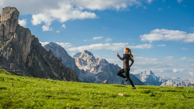 一个快乐的女人在草地上慢跑，背景是山脉视频素材