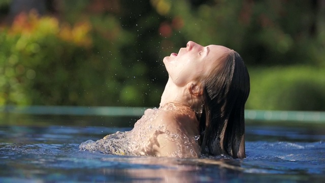 年轻性感的女人从水里出来，湿头发呼吸空气。自由和享受的概念视频下载