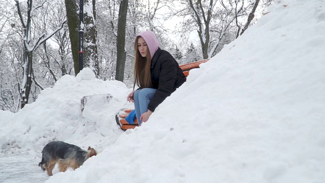一个年轻的女孩坐在长椅上抽烟，在一个冰雪覆盖的公园里。视频下载