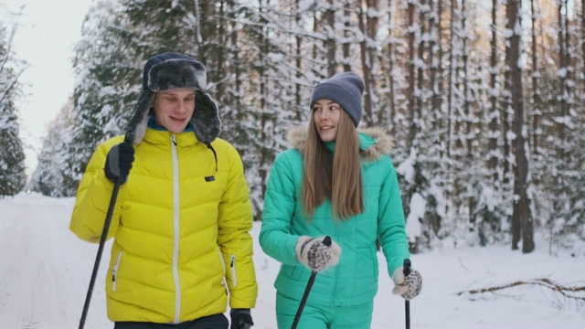 微笑的男人在冬天的夹克在森林滑雪慢动作与他爱的妻子。健康的生活方式。年轻的夫妇视频下载