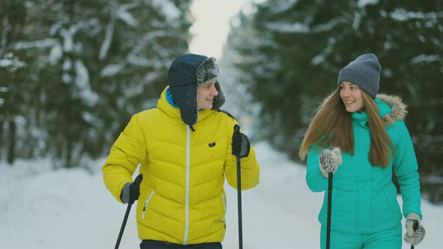 一个穿黄色夹克的男人和一个穿蓝色连身裤的女人在冬天的树林里慢动作滑雪视频下载