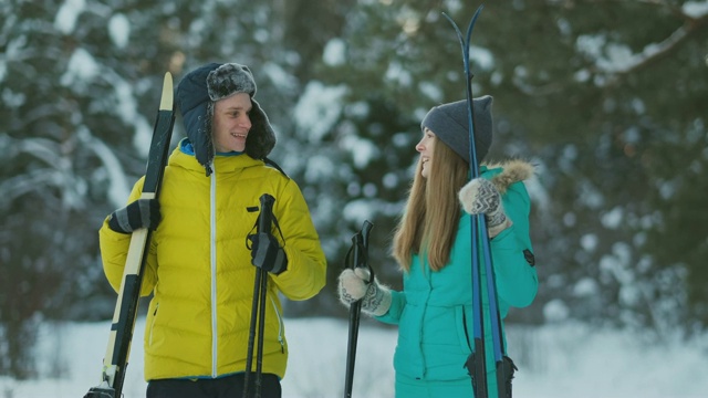 全身像活跃的年轻夫妇享受滑雪在下雪的冬天森林，关注微笑的女人在前面，复制空间视频下载
