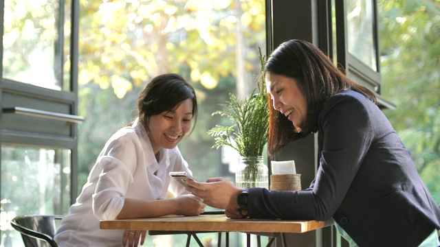 两个女性朋友在咖啡馆一起分享智能手机视频下载