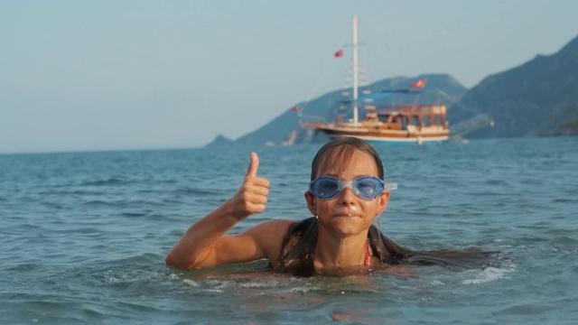 女孩从海里出来，露出拇指。快乐的孩子在海里洗澡视频下载