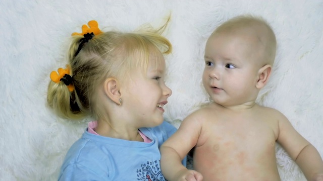 一个6个月大的男孩和一个4岁的女孩躺在家里的白色床单上的特写。视频素材