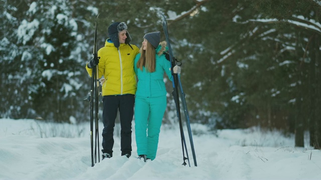全身像关心年轻男子帮助受伤的女朋友在冬季森林滑雪步行视频下载