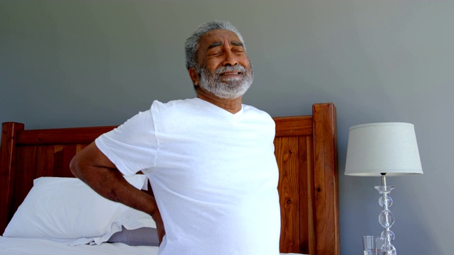 前视图的高级黑人男子坐在床上持有较低的背部在一个舒适的4k家视频下载
