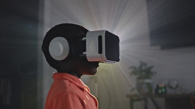 非裔美国男孩SLO戴着VR头盔，在投影仪的光线下站成一个侧面。视频素材