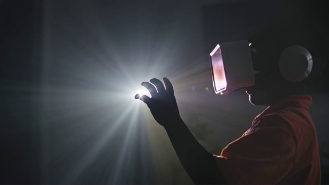 非裔美国男孩戴着虚拟现实头盔，把手伸到投影仪的灯光下。视频素材