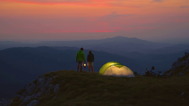 慢镜头:在一个寒冷的夏夜，一对无忧无虑的夫妇在他们的帐篷边聊天。视频素材