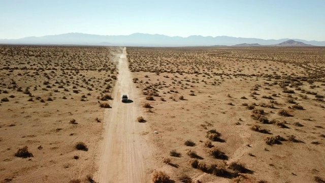 鸟瞰图:在沙漠景观中的土路上朝着相机行驶的车辆视频下载