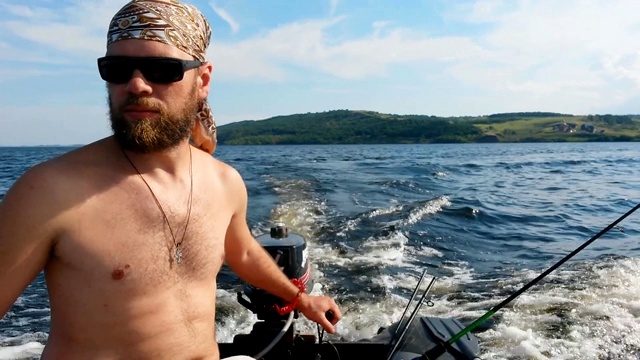 一个戴眼镜、留着胡子、戴着大手帕的男人夏日里驾着摩托艇在河上航行。视频下载