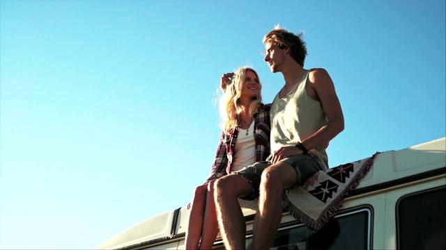 一对夫妇坐在车顶上，背靠晴朗的天空视频素材