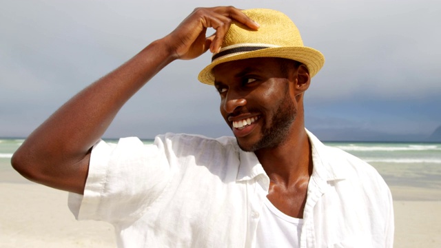 一个戴着帽子的男人在一个晴朗的日子里站在海滩上视频素材