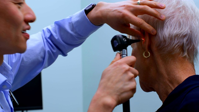 年轻的亚洲男医生在4k诊所用耳镜检查一位老年病人视频下载