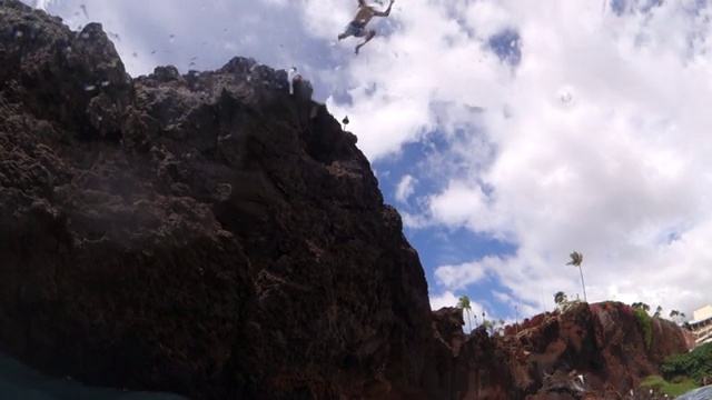 广角镜头:一个人从岩石上跳到蓝色的海水里视频下载