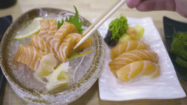 用筷子夹住三文鱼生鱼片的手放在盘子上。吃日本菜。顶视图开枪。视频素材