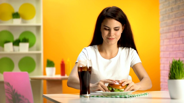 微笑的黑发女人从盘子里吃美味的汉堡，快餐店视频素材