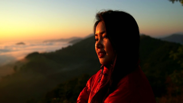 一个女性徒步旅行者的剪影在山与雾海在山谷在日落时分。视频素材