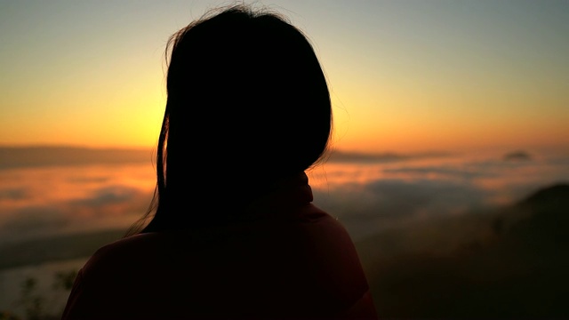 一个女性徒步旅行者的剪影在山与雾海在山谷在日落时分。视频素材