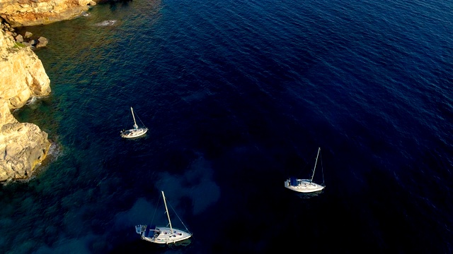 西班牙米诺卡湾的帆船鸟瞰图。美丽的海滩和地中海的蓝色海水。在陆地上，只有岩石和草的自然。视频素材
