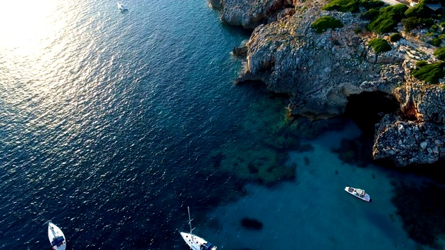 在西班牙米诺卡湾，一架无人机鸟瞰帆船。美丽的海滩和地中海的蓝色海水。在陆地上，只有岩石和草的自然。视频素材