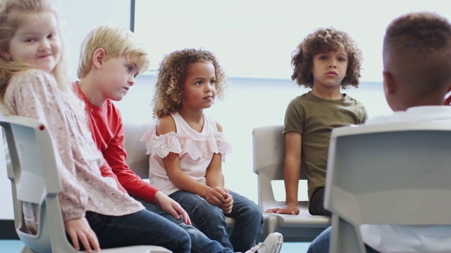 多民族学校的孩子坐在婴儿学校教室的椅子上，近距离观看视频素材