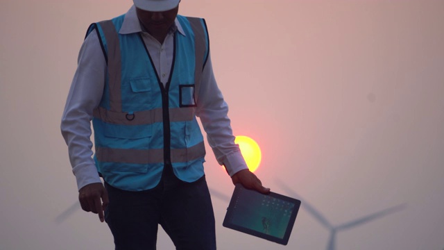 一名男性工程师在风力涡轮机前拿着平板电脑视频素材