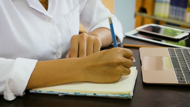 年轻的亚洲女性在笔记本上写作，在大学图书馆做研究，学习教育和学校理念视频素材