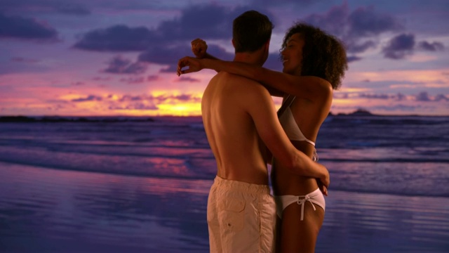 浪漫的夫妇在海滩上看日落的肖像。一对年轻的夫妇在海滩上互相拥抱，观看海浪。4 k视频下载