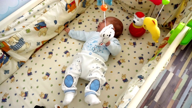 快乐微笑的宝宝躺在婴儿床上玩音乐旋转木马玩具。视频下载