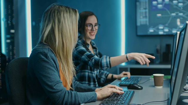 两位女IT程序员在数据中心系统控制室的台式机上工作。年轻的专家团队在软件和硬件开发，做编码视频素材