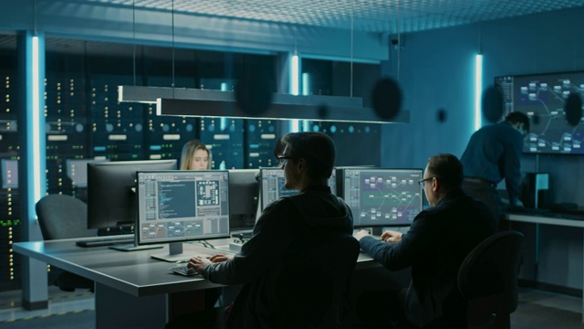 在数据中心控制室的台式计算机上工作的IT程序员团队。年轻的专业人士写复杂的编程代码语言。高架移动摄像机拍摄视频素材