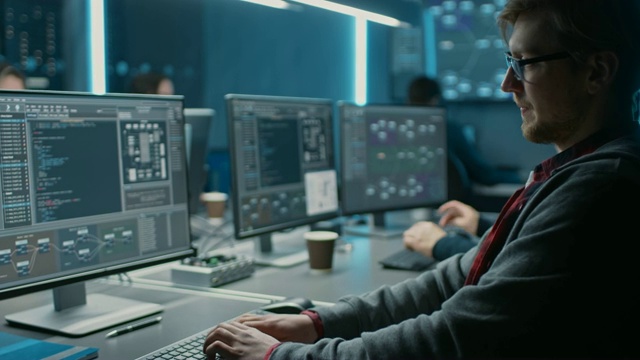聪明的男性IT程序员，在数据中心技术系统控制室的台式电脑上工作。用编码语言编程的年轻专业人员团队视频素材