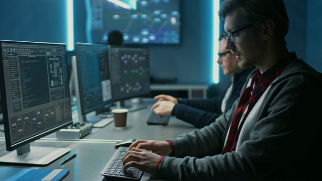 在数据中心系统控制室的台式电脑上工作之前，聪明的男性IT程序员伸展并热身双手。年轻的专业人员编程复杂的代码团队视频素材