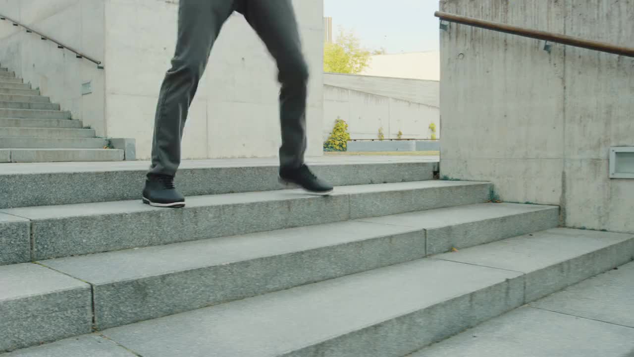 一个长头发的快乐的年轻人走下楼梯时积极地跳舞。他穿着一件棕色的皮夹克。场景拍摄于商业中心旁边的城市混凝土公园。阳光明媚的。视频素材
