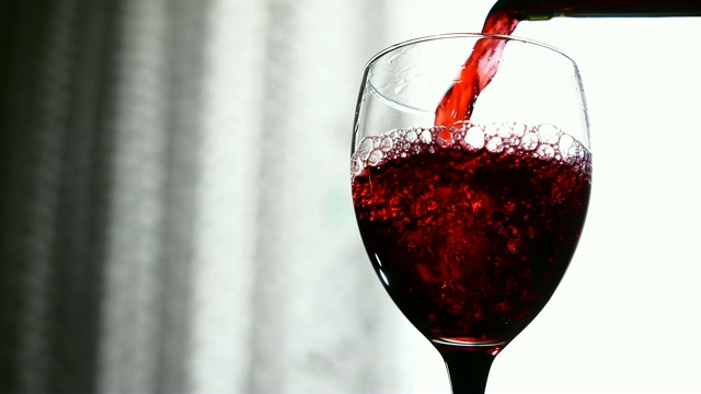 在灯光背景下，红酒倒入玻璃杯中视频素材
